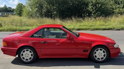 Side profile of red Mercedes-Benz SL R129 convertible parked on a quiet road